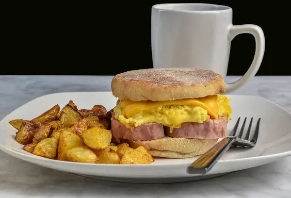 Konserve jambon, çırpılmış yumurta ve peynirli İngiliz çöreği, yanında patates kızartması ve kahve.