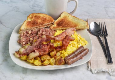 Çırpılmış yumurta, domuz pastırması, sosis, yanında mısır gevreği ve patates kızartması.,