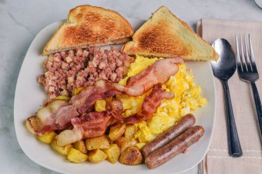 Yağda yumurta, patates kızartması ve sosis ve domuz pastırması ile servis edilen mısır kıyması., 