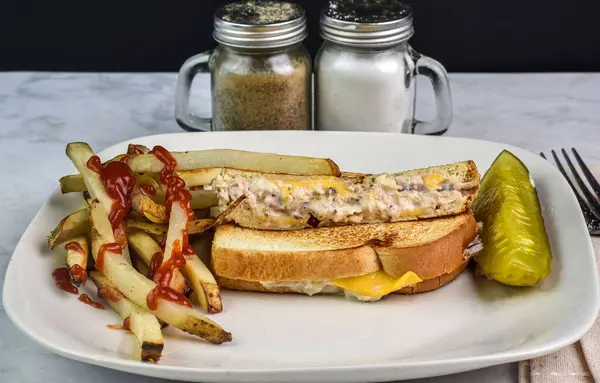 Patates kızartmasıyla servis edilen ton balıklı sandviç. ve turşu.