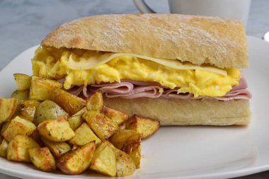 Çırpılmış yumurta, jambonlu ve peynirli sandviç ve yanında patates kızartması.