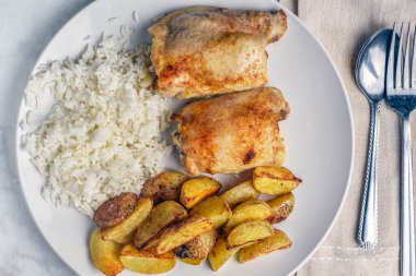 Pirinç ve patates dilimleri ile servis edilen tavuk butları., 