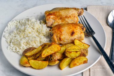 Pirinç ve patates dilimleri ile servis edilen tavuk butları.,