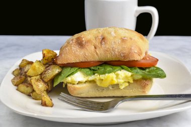 Çırpılmış yumurta üstü, yanında patates kızartması ve ciabatta rulosuyla servis edilen domatesli.