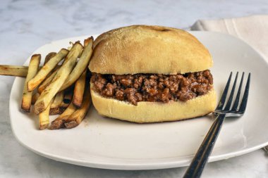 Ciabatta rulosunun üzerinde patates kızartması ile servis edilen kıymalı sandviç.