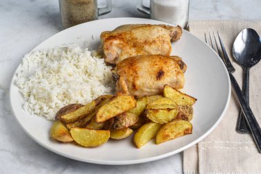 Baharatlı patates ve pilav ile servis edilen tavuk butları.