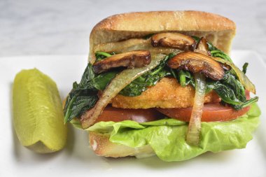 Sotelenmiş soğan, mantar ve domates ve marulun üzerinde dinlenen ıspanak ile ciabatta rulosunda servis edilen tavuk göğsü.