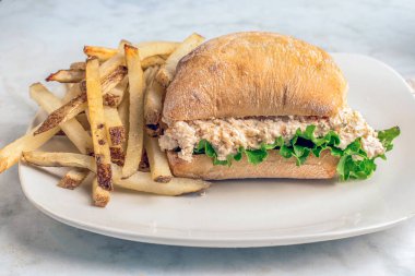 Ciabatta rulosunun üzerinde marullu tavuk salatası ve ev yapımı patates kızartması..