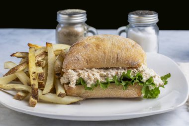 Ciabatta rulosunun üzerinde marullu tavuk salatası ve ev yapımı patates kızartması..