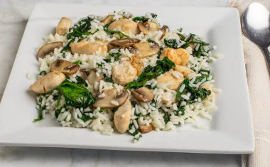 Beyaz pirinç sotelenmiş ıspanak ve mantarla servis edilir ve üstü tavuk ısırıklarıyla kaplanır.,