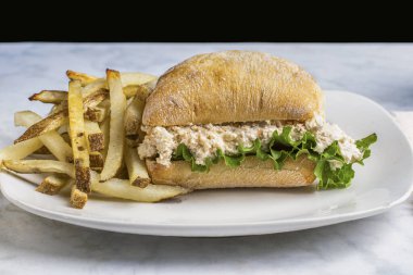 Ciabatta rulosunun üzerinde marullu tavuk salatası ve ev yapımı patates kızartması..