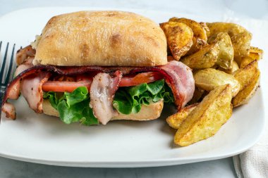 Ciabatta rulosunda yanında patates dilimleri ile servis edilen domates ve pastırma.,