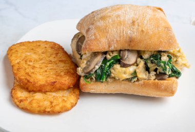 Sotelenmiş mantarla çırpılmış yumurta ve ciabatta rulosu üzerinde ıspanak haşlanmış patatesle servis edilir.,