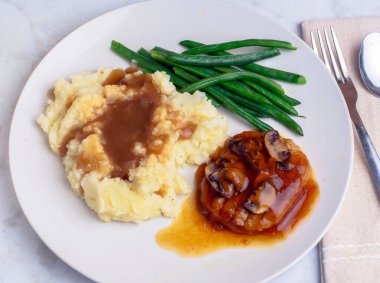 Soğan soslu salisbury bifteği ve patates püresiyle servis edilen mantarlar.