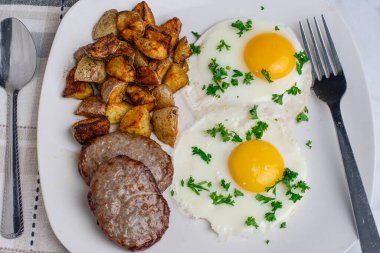İki sahanda yumurta ve maydanozlu sosisli börek ve patates kızartması.