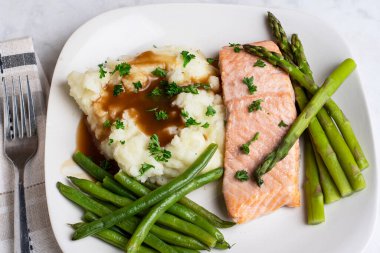 Fırında somon, patates püresi ve maydanozlu sos üstü yeşil fasulye ve kuşkonmazla servis edilir.