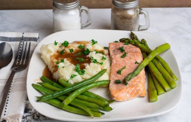 Fırında somon, patates püresi ve maydanozlu sos üstü yeşil fasulye ve kuşkonmazla servis edilir.