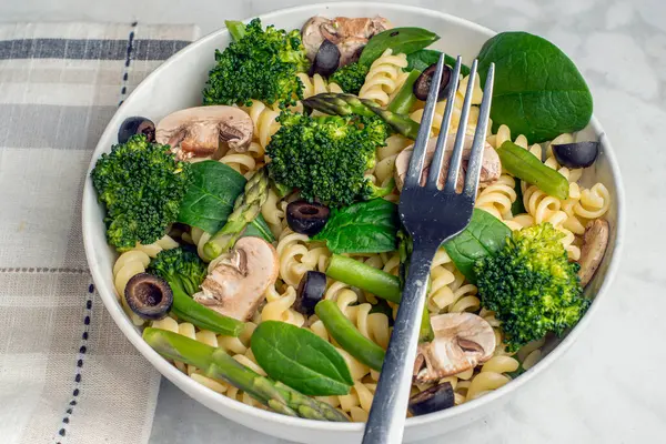 Mantar, zeytin, ıspanak ve brokoli ile servis edilen rotini makarna.