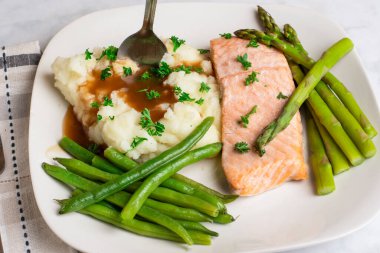 Fırında somon, patates püresi ve maydanozlu sos üstü yeşil fasulye ve kuşkonmazla servis edilir.