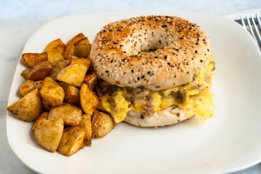 Çırpılmış yumurta, yanında patates kızartmasıyla servis edilen simit üzerine sosis.