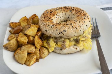 Çırpılmış yumurta, yanında patates kızartmasıyla servis edilen simit üzerine sosis.