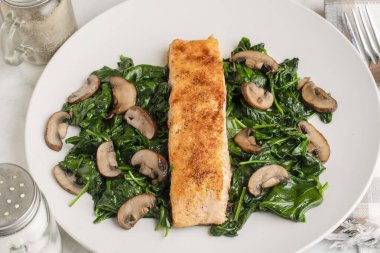 Baharatlı somon balığı sotelenmiş ıspanak ve mantarla servis edilir.