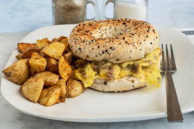 Çırpılmış yumurta, yanında patates kızartmasıyla servis edilen simit üzerine sosis.