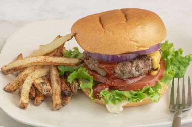 Hamburger, marullu domates ve soğanlı çörek ve patates kızartması.