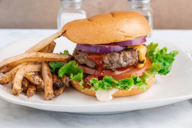 Hamburger, marullu domates ve soğanlı çörek ve patates kızartması.