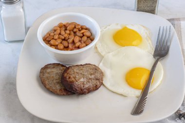 İki kızarmış yumurta, iki sosisli börek ve bir kase fırında fasulye.
