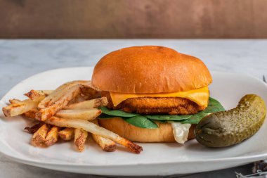  Patates kızartması ve turşuyla servis edilen peynirli çörekli tavuk köftesi., 