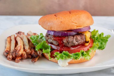 Hamburger, marullu domates ve soğanlı çörek ve patates kızartması.
