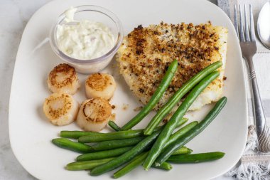 Tavada kesilmiş deniz tarağı ve haşlanmış yeşil fasulyeyle servis edilen mezgit.