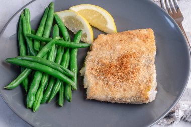 Haşlanmış taze fasulyeyle servis edilen kızarmış morina balığı. 