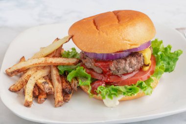 Hamburger, marullu domates ve soğanlı çörek ve patates kızartması.