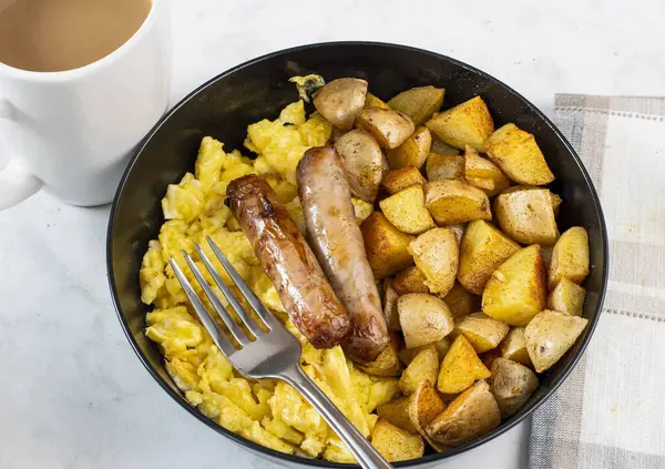 Bir fincan kahveyle servis edilen çırpılmış yumurta ve patates kızartmasıyla sosis halkaları.