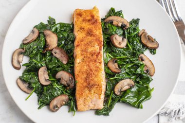 Baharatlı somon balığı sotelenmiş ıspanak ve mantarla servis edilir.