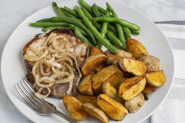 Sotelenmiş soğanlı domuz pirzolası sotelenmiş yeşil fasulye ve patates dilimleri ile servis edilir.