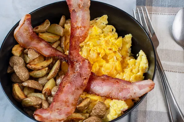 Çırpılmış yumurta ve patates kızartması. Üstü bocon ile servis edilmiş.