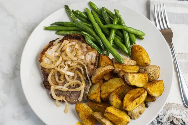 Sotelenmiş soğanlı domuz pirzolası sotelenmiş yeşil fasulye ve patates dilimleri ile servis edilir.