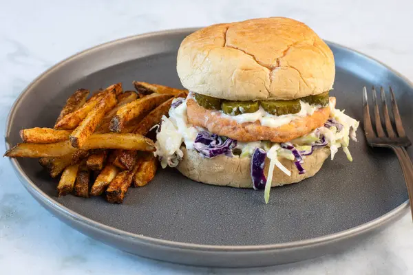 Lahana salatalı somon burger ve turşu ve mayonezli üstü. Patates kızartması ile servis edilir.