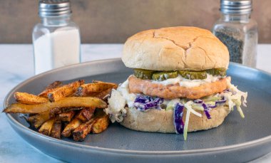 Lahana salatalı somon burger ve turşu ve mayonezli üstü. Patates kızartması ile servis edilir.