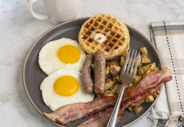 Erimiş tereyağlı kızarmış yumurta, domuz pastırması, sosis ve patates kızartması ile servis edilen şurup.