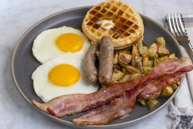 Erimiş tereyağlı kızarmış yumurta, domuz pastırması, sosis ve patates kızartması ile servis edilen şurup.