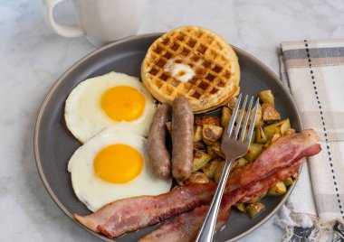 Erimiş tereyağlı kızarmış yumurta, domuz pastırması, sosis ve patates kızartması ile servis edilen şurup.