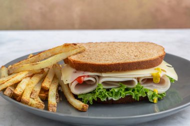 Marul ve peynirli dilimlenmiş hindi, yanında patates kızartması ve buğday ekmeği ile servis ediliyor.