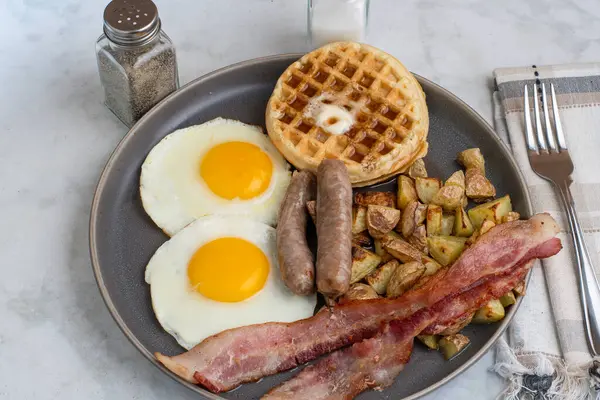 Erimiş tereyağlı kızarmış yumurta, domuz pastırması, sosis ve patates kızartması ile servis edilen şurup.