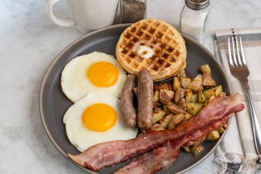 Erimiş tereyağlı kızarmış yumurta, domuz pastırması, sosis ve patates kızartması ile servis edilen şurup.