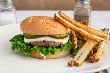  Peynirli ve turşulu hamburger üstü, patates kızartmasıyla servis edilen susamlı ekmek.