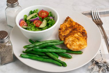 Baharatlı tavuk göğsü, salata ve yeşil fasulye ile servis edilir..